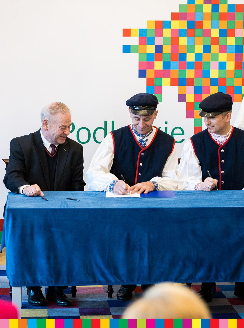 Trzech mężczyzn siedzi przy stole i podpisuje umowy.