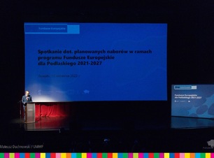 Wielki ekran ze slajdem oraz mężczyzna stojący za mównicą.