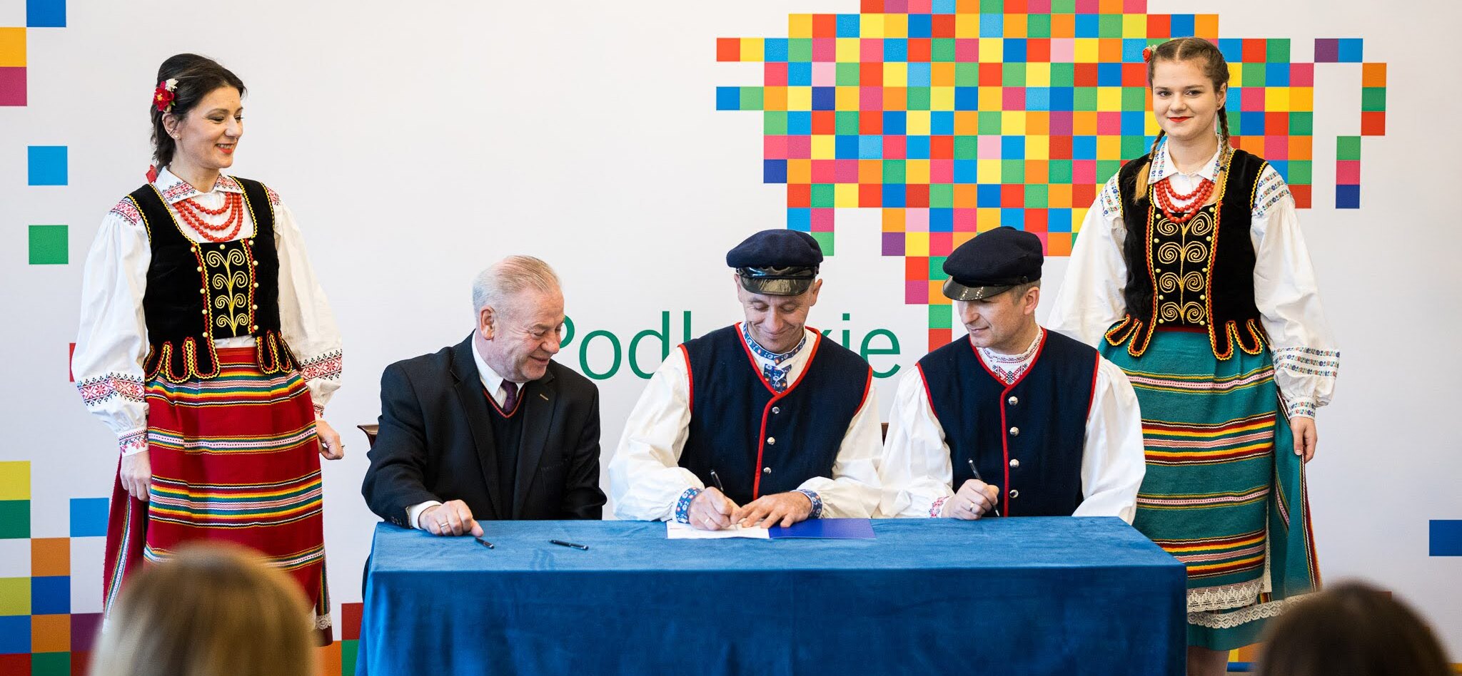 Trzech mężczyzn siedzi przy stole i podpisuje umowy.