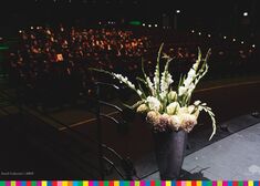Kwiaty w wazonie ustawione na scenie, w tle uczestnicy wydarzenia siedzący na widowni