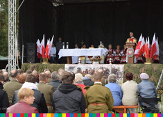 Uczestnicy wydarzenia siedzą tyłem, na scenie duchowny który mówi do mikrofonu