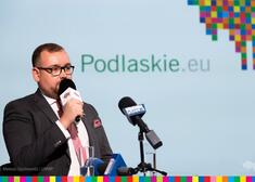 Wicemarszałek Łukaszewicz mówi do mikrofonu, za nim widoczne logo województwa i nazwa nowej strony