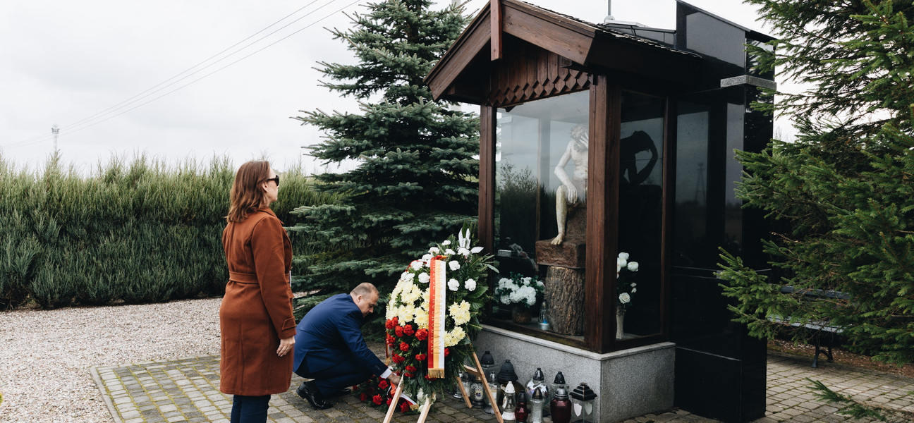 Mężczyzna składa kwiaty przed kapliczką, mężczyzna stoi