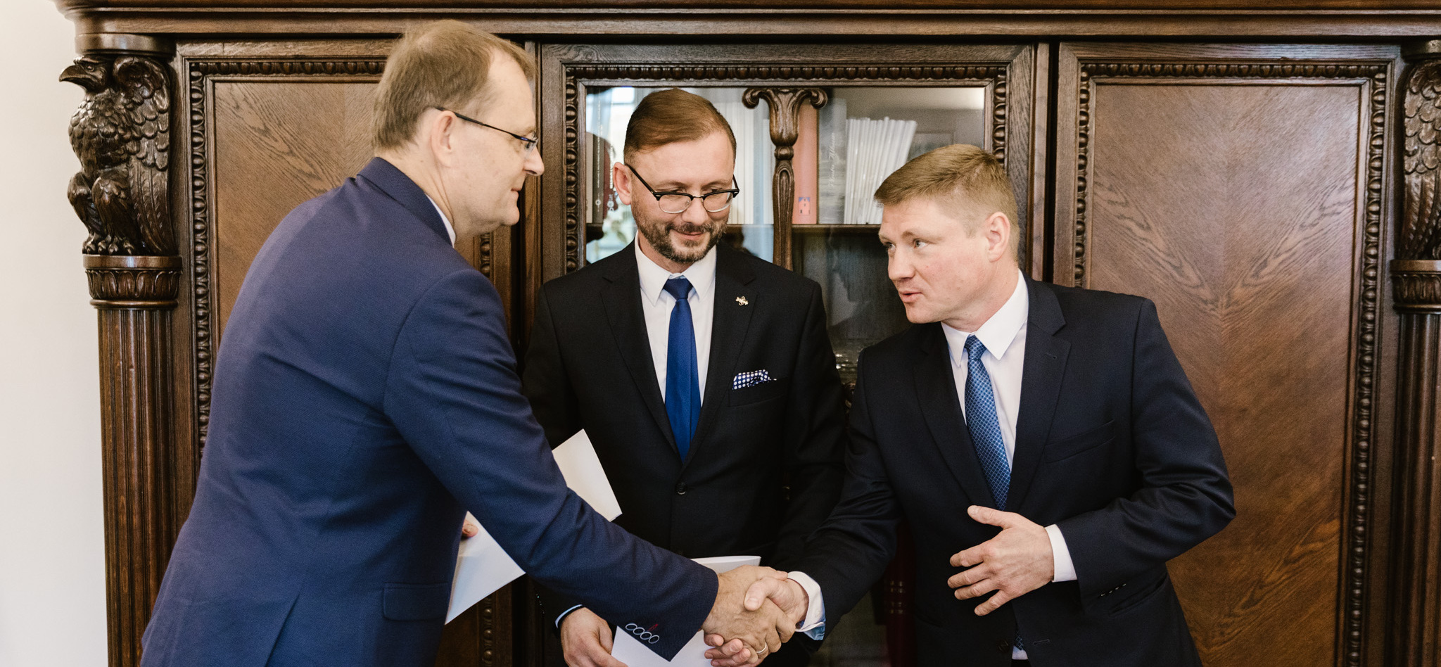 Trzej mężczyźni w garniturach podają sobie ręce. Wśród nich jest członek zarządu Marek Malinowski