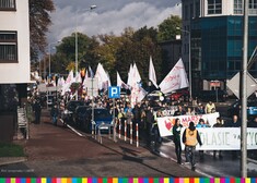 Uczestnicy marszu idą ulicami miasta. Na początku idzie kilka osób, w tym marszałek Kosicki