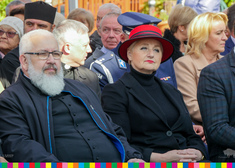 Uczestnicy wydarzenia, na pierwszym planie mężczyzna i kobieta w czerwonym kapeluszu