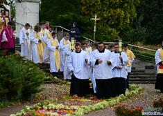 Duchowni i ministranci idą w procesji po dywanie z kwiatów
