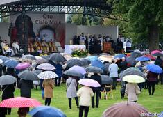 Uczestnicy wydarzenia pod parasolkami stoją przed ołtarzem polowym