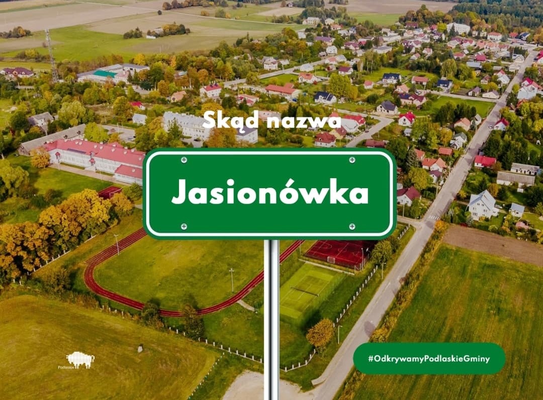 zielona tablica z nazwą miejscowości Jasionówka na tle zdjęcia miejscowości z lotu ptaka