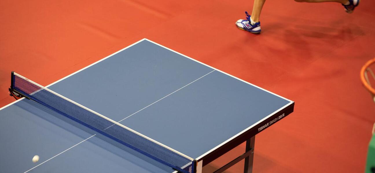Granatowy stół do tenisa, u góry widoczna noga zawodnika