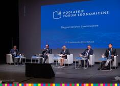 Wicemarszałek Łukaszewicz w towarzystwie uczestników na tle ekranu z logo Podlaskiego Forum Ekonomicznego