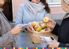 Kobieta w błękitnym płaszczu trzyma skrzynkę z jabłkami