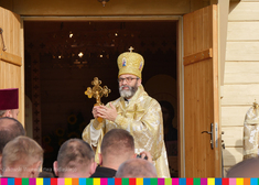 Arcybiskup Jakub przed kaplicą trzyma w dłoniach krzyż.