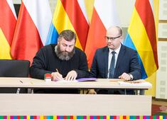 marszałek Artur Kosicki oraz ksiądz prawosławny siedzą przy stole i podpisuja umowę