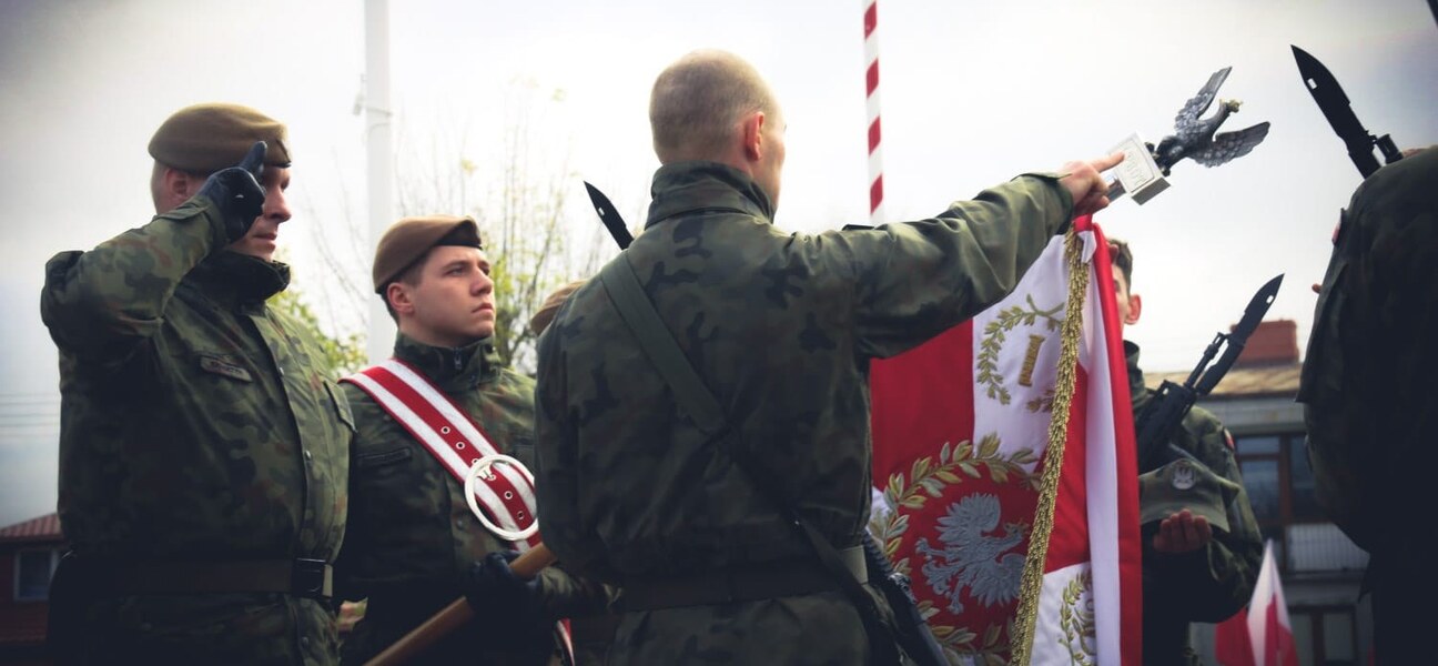 Mężczyźni w mundurach wojskowych stoją przy sztandarze