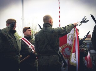 Mężczyźni w mundurach wojskowych stoją przy sztandarze
