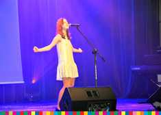 Nastolatka w białej sukience śpiewa na scenie