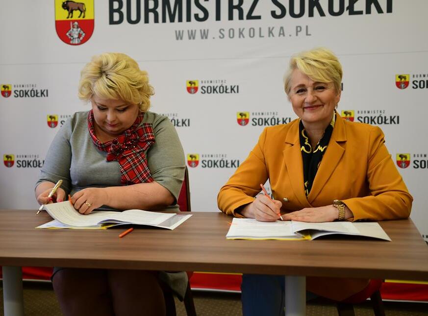 Dwie kobiety o blond włosach na tle ścianki z logo burmistrza Sokółki