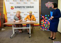 Wiesława Burnos siedzi przy wstole razem z kobietą podczas podpisania umowy