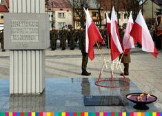 Pomnik na placu, obok niego flagi Polski