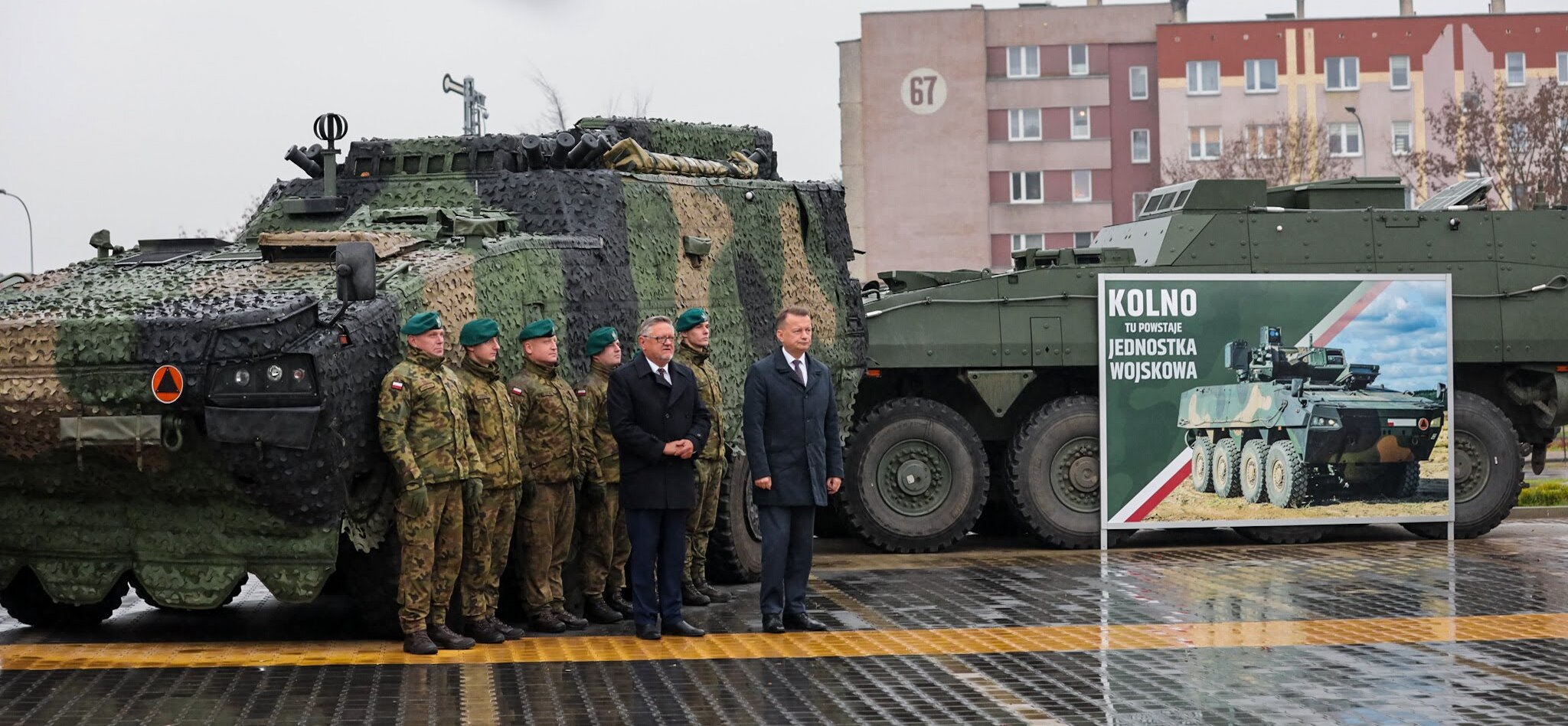Mężczyźni oraz wojskowi stoją na tle czołgów
