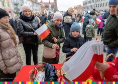 Uczestnicy uroczystości na placu w flagami Polski