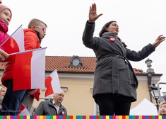 Kobieta z uniesionymi rękoma, obok dzieci z flagami Polski