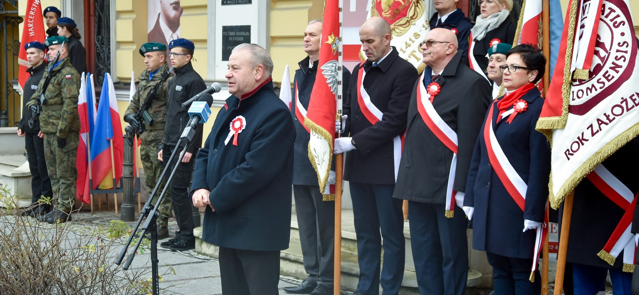 Wicemarszałek Marek Olbryś przemawia do mikrofonu na tle osób trzymających sztandar