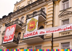 Godło Polski i herb Łomży zawieszone na balkonie kremowego budynku