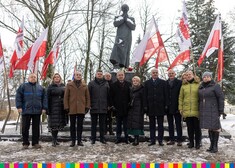Grupa ludzi przed pomnikiem ks. Popiełuszki, w tle flagi biało-czerwone