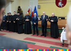 Osoby świeckie oraz duchowne stoją w rzędzie w dużej sali konferencyjnej
