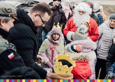 Wicemarszałek Sebastian Łukaszewicz przekazuje upominki dzieciom. W tle stoi osoba przebrana za Mikołaja oraz duża grupa ludzi