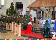Chór wojskowy, obok szopka bożonarodzeniowa.