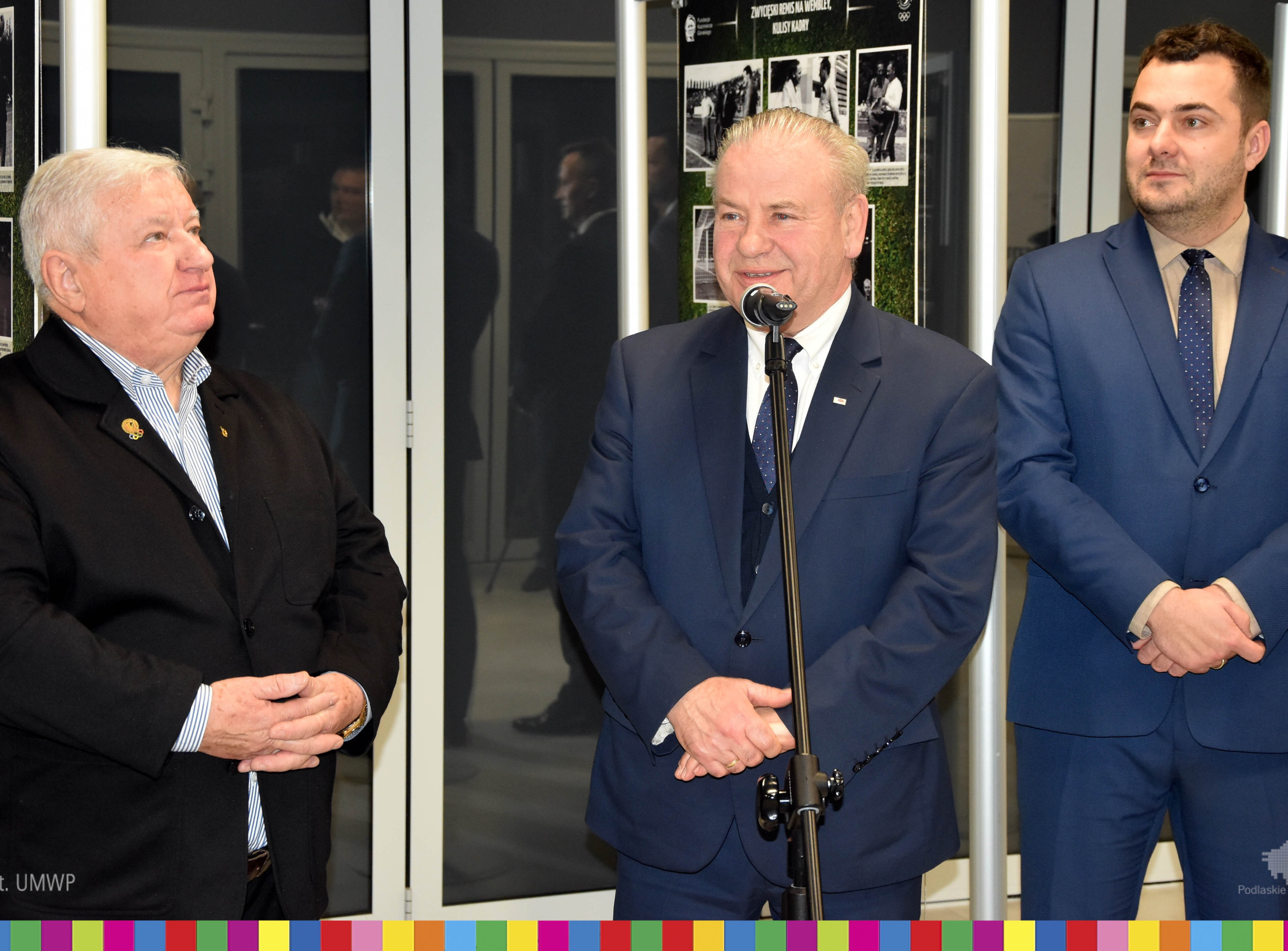 wicemarszałek Marek Olbryś stoi przy mikrofonie, obok niego stoją dwaj mężczyźni