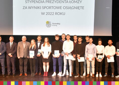 stypendyści pozują do wspólnego zdjęcia, za nimi znajduje się wyświetlony napis: Stypendia Prezydenta Łomży za Wyniki Sportowe Osiągnięte w 2022 roku 