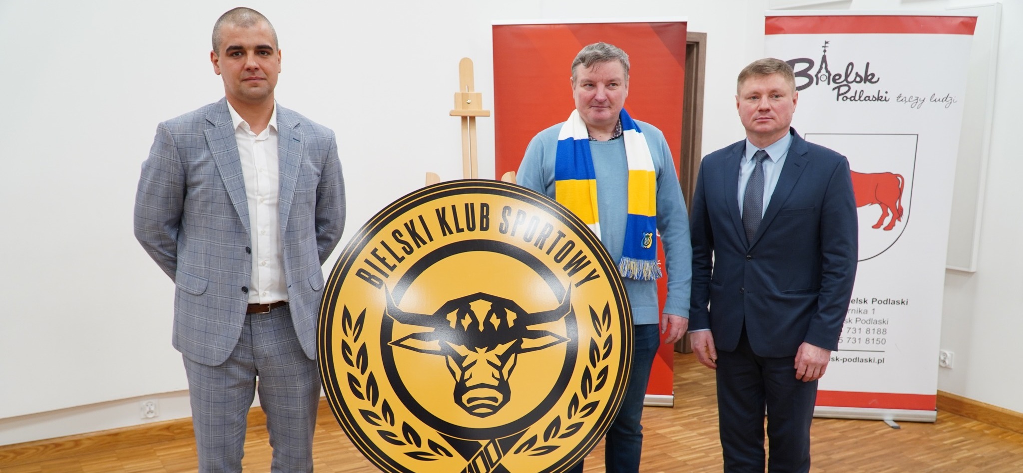 Trzech mężczyzn przy logo bielskiego klubu sportowego