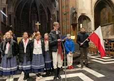 śpiewające dzieci, jeden z chłopców trzyma polską flagę