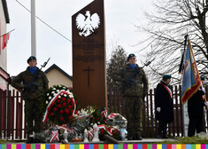 pomnik przy którym stoją żołnierze, przed pomnikiem leżą wieńce kwiatowe 