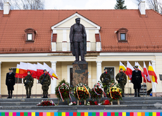 Wieńce złożone przy pomniku Józefa Piłsudskiego, służby mundurowe, za nimi flagi