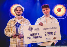 Przemek Piotrowski trzyma czek na kwotę 2,5 tys. zł, obok niego stoi mężczyzna trzymający statuetkę 