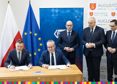 dwóch mężczyzn siedzi przy biurku podczas podpisania listu intencyjnego, przy nich stoją: marszałek Artur Kosicki oraz wicepremier Sasin