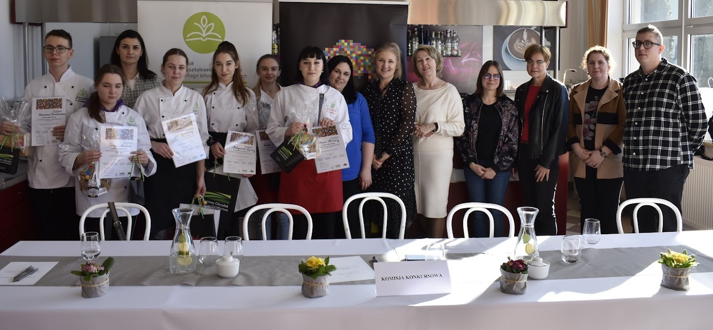 Młodzi kucharze stoją z dyplomami w rękach, obok nich znajduje się sześć kobiet i jeden mężczyzna
