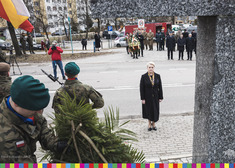 Wieslawa Burnos, członek zarządu stoi przed krzyżem na baczność, Przy pomniku żołnierze trzymają wartę. W oddali widać tłum ludzi