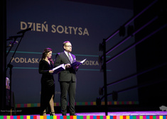 Red. Urszula Sokołowska oraz wicemarszałek Sebastian Łukaszewicz stoją na scenie i trzymają w dłoni otwarte teczki