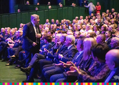 Europoseł Krzysztof Jurgiel stoi przed tłumem osób siedzących na widowni w operze
