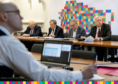 Czterech starszych Panów siedzi za stołem na tle loga Województwa Podlaskiego