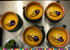 Filiżanka z zupą kremem, ozdobiona fioletowymi płatkami i ziemniaczkiem