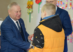 Wicemarszałek Marek Olbryś gratuluje chłopakowi w towarzystwie mężczyzny w garniturze