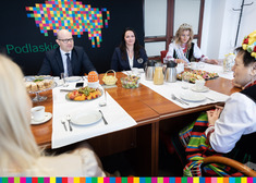Kilka osób siedzi za zastawionym stołem. W tle logo województwa - żubry z kolorowych pikseli.