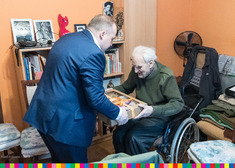 Mężczyzna przekazuje paczkę starszemu człowiekowi siedzącemu na wózku inwalidzkim